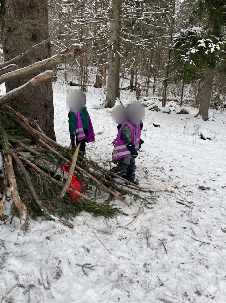 Barn bygger gapahuk av kvister i vinterskogen